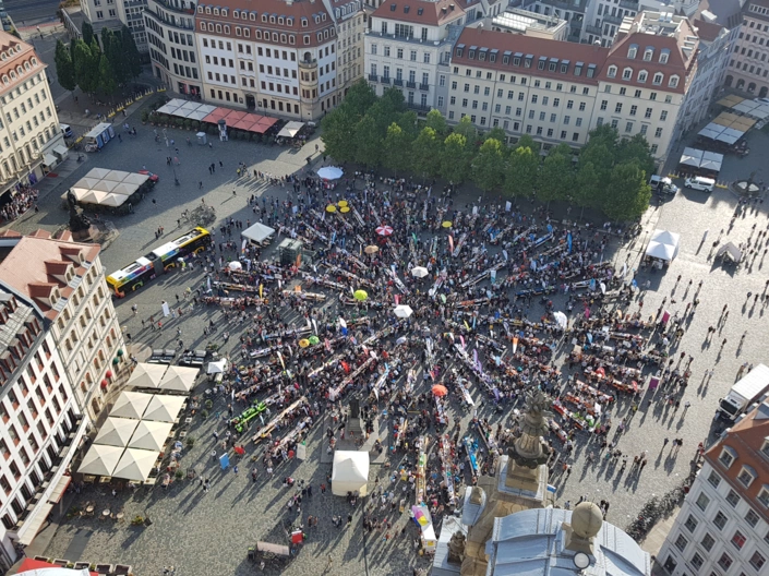 Auf dem Dresdner Neumarkt stehen sternförmig Tische und Bänke, zahlreiche Menschen halten sich dort auf.