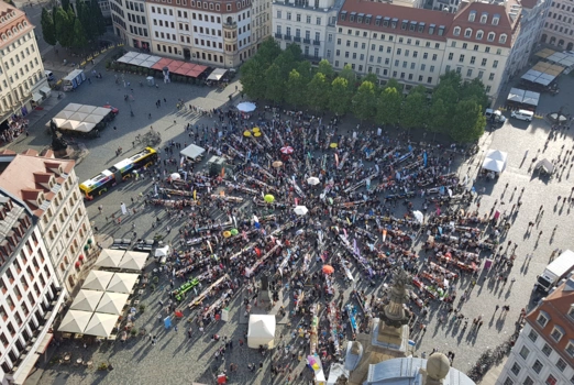 Auf dem Dresdner Neumarkt stehen sternförmig Tische und Bänke, zahlreiche Menschen halten sich dort auf.