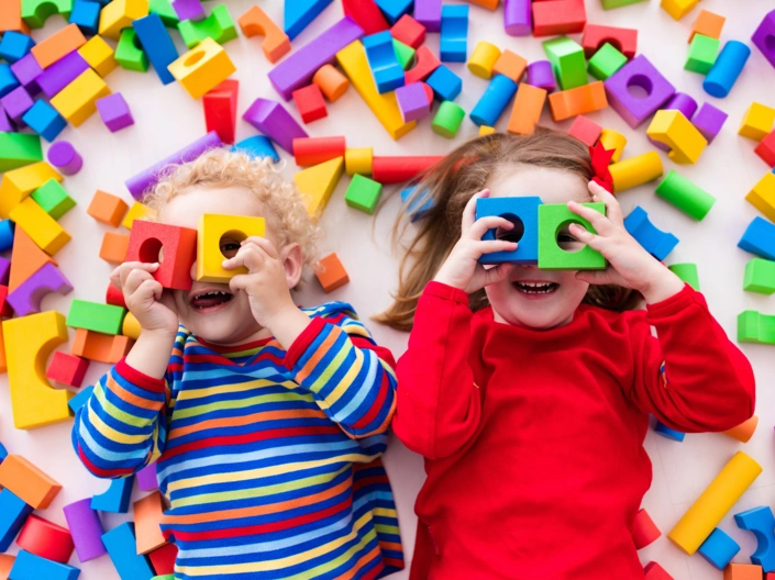 Zwei Kinder liegen zwischen Bausteinen und gucken durch welche hindurch.