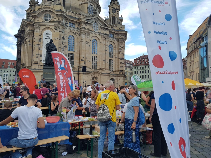 Tische, Bänke und Menschen bei Gastmahl am Dresdner Neumarkt, im Hintergrund die Frauenkirche.