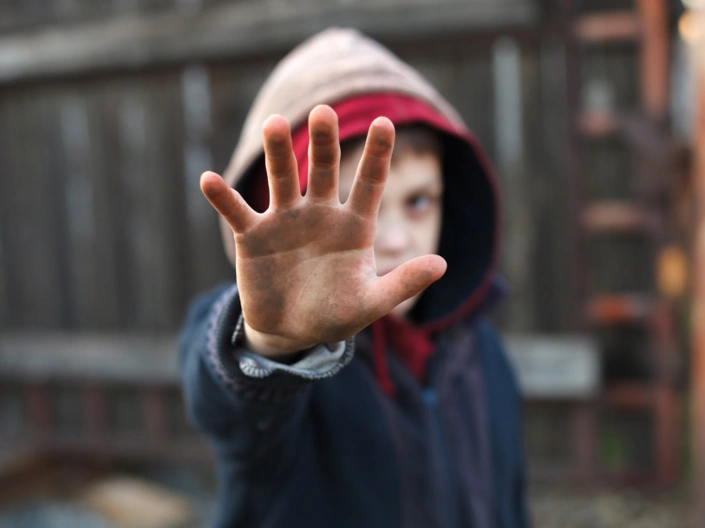 Ein ärmlich gekleideter Junge hält seine beschmutzte Hand abwehrend in Richtung des Betrachters.