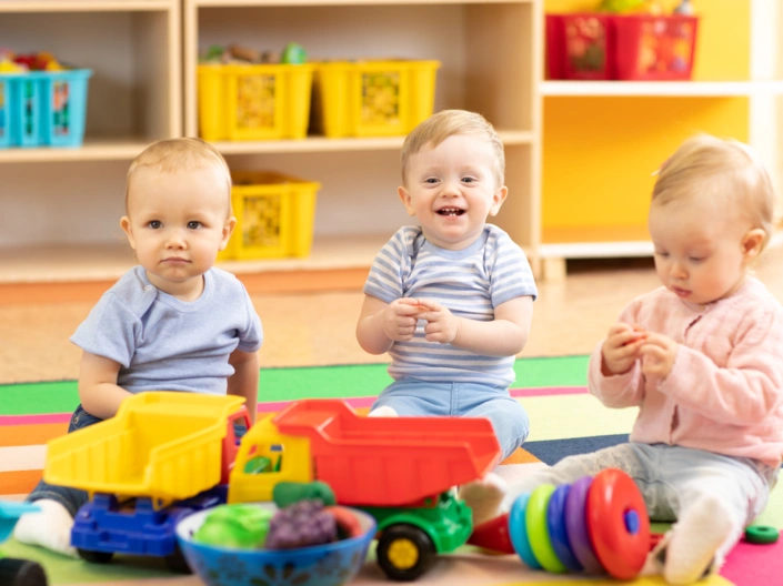 Drei Krippenkinder sitzen auf dem Boden uns spielen.