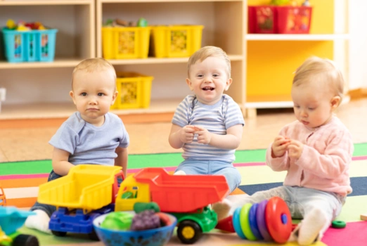 Drei Krippenkinder sitzen auf dem Boden uns spielen.