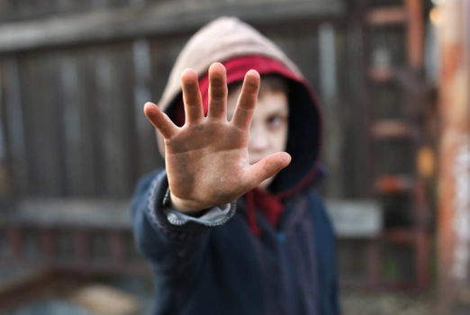 Ein ärmlich gekleideter Junge hält seine beschmutzte Hand abwehrend in Richtung des Betrachters.