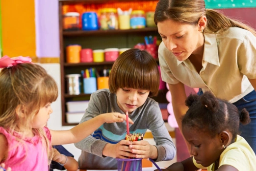 Drei Grundschüler und eine Lehrerin räumen Buntstifte in einen Becher.